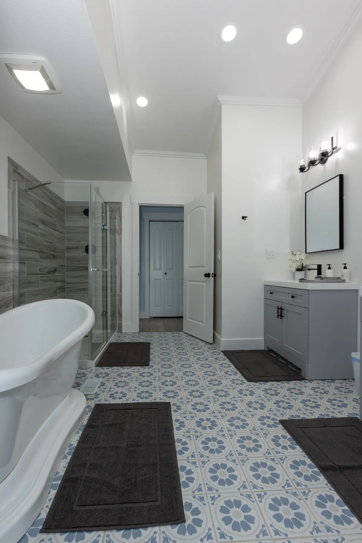 A modern, tranquil bathroom featuring a freestanding bathtub, double sink vanity, glass shower enclosure, and decorative floor tiles. The space is bright, airy, and exudes spa-like comfort.