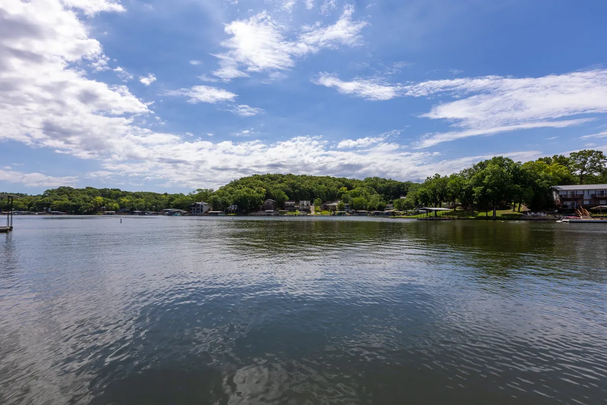 A broad, serene lakescape with calm waters, lush green trees, and homes dotting the shoreline at sunset. The ambiance is relaxed and inviting, ideal for boating, fishing, or simply taking in the view, and the scene captures the feeling of exploring local coves or enjoying nature from your vessel.
