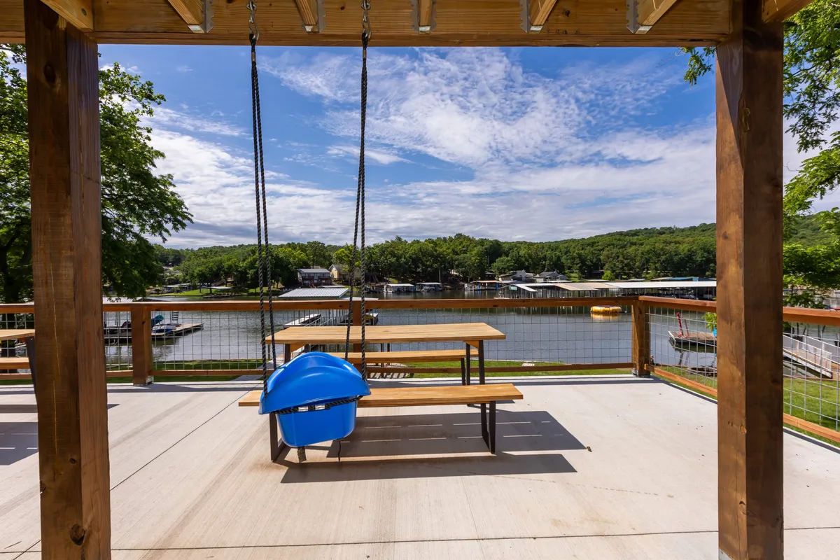 A tranquil lakeside setting featuring a wooden swing and a picnic table, both positioned to take full advantage of the captivating water view. The area is surrounded by greenery, and the swing invites guests of all ages to relax or socialize while enjoying beautiful sunsets or watching boats pass by.