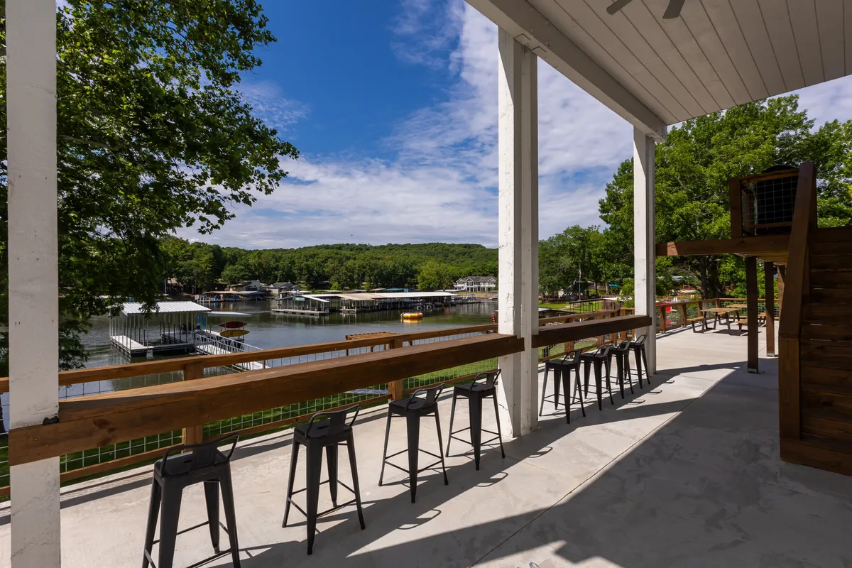 A scenic outdoor bar seating area overlooks the water, framed by surrounding greenery. The arrangement invites guests to relax, socialize, and enjoy panoramic lake views, fostering a sense of community and outdoor leisure.