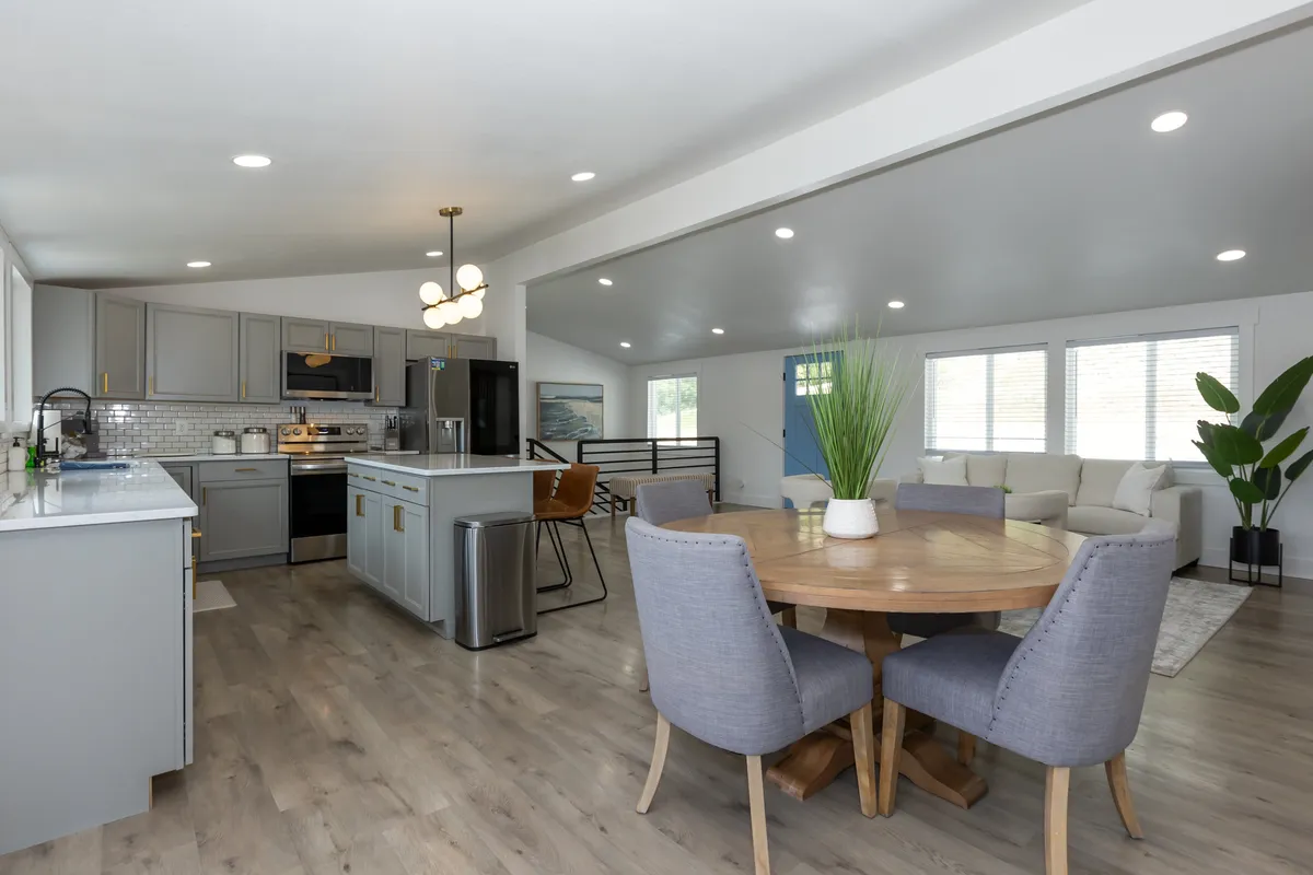 A spacious open-concept living area featuring a kitchen island, dining table, and comfortable sofa. Large windows flood the space with natural light and offer glimpses of the lake beyond, creating a welcoming environment perfect for group gatherings and family meals.
