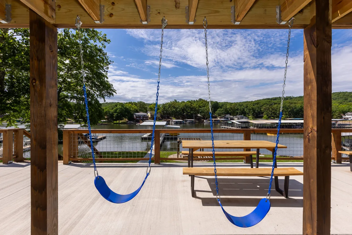 The hero image showcases an inviting lakefront backyard with a swing set overlooking the water, picnic tables ready for outdoor meals, and tranquil views of Lake Ozark. The scene captures children swinging, families gathered at picnic tables, and the sun setting over the water, highlighting a setting perfect for relaxation and togetherness.