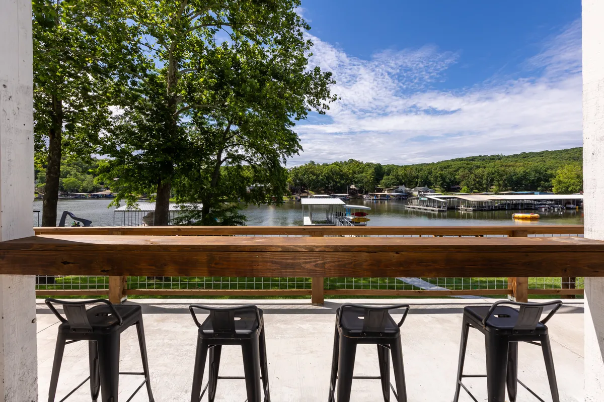A scenic outdoor bar seating area overlooking the lake, with lush greenery providing a serene backdrop. The bar seating is positioned to maximize the experience of socializing and enjoying picturesque lake views, especially during sunset.